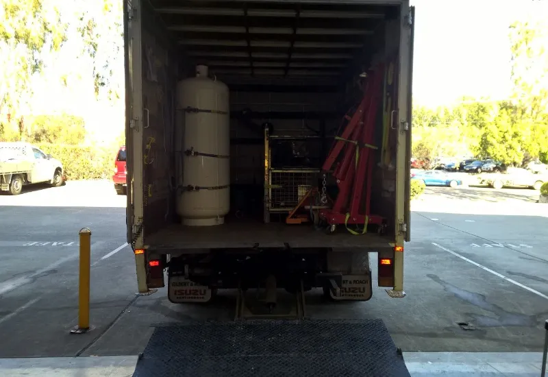 A large white gas cylinder and red lifting equipment securely loaded inside the back of an Isuzu truck, ready for transport in an industrial or warehouse setting.
