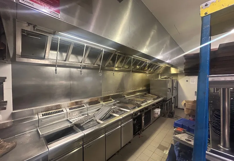 Commercial kitchen with stainless steel appliances, deep fryers, grills, and ventilation hoods, showing a professional setup designed for high-volume cooking and fire safety compliance.