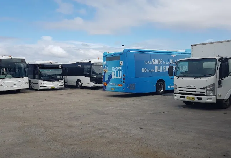 Several buses and a truck parked in an open lot under a partly cloudy sky