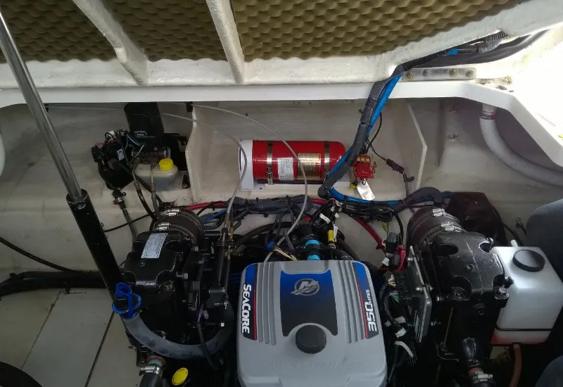 Open boat engine bay with a MerCruiser 350 MAG SeaCore inboard engine, wiring and hoses, and a red automatic fire extinguisher mounted aft.