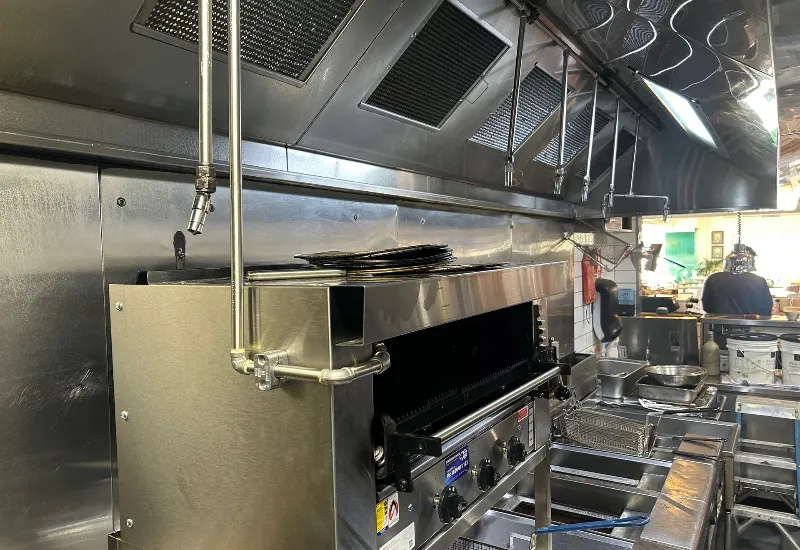 Commercial kitchen with stainless steel cooking equipment, including a grill and fryers, under a ventilation hood system with integrated fire suppression nozzles for safety and efficient operation.
